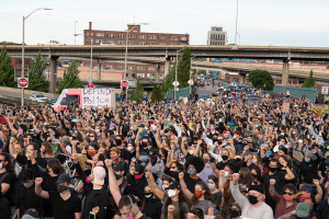 Hundreds of masked people marching across the Morrison Bridge with fists raised, and a pink truck in the background reading "Defund Police"