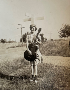 Vintage black and white photo of a young woman standing in a rural road and holding a guitar.