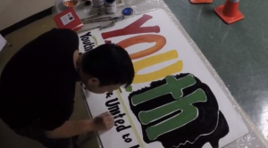 young man painting a sign that says YOUTH in rainbow letters