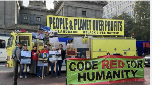 Image of PEST's "World on Fire" Truck An image of PEST's "World on Fire" truck with banners reading "People and Planet Over Profit" and "Code Fred For Humanity"