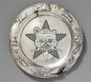 A silver 23rd anniversary plate with the Self Help Radio logo within.