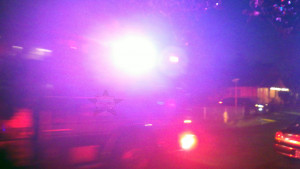 An emergency vehicle speeding past in the night, red lights flashing, with the Self Help Radio logo inexplicably on the vehicle's side.